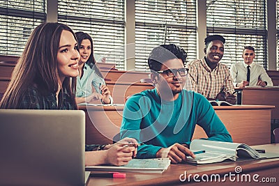 Multinational group of cheerful students taking an active part in a lesson while sitting in a lecture Hall. Stock Photo