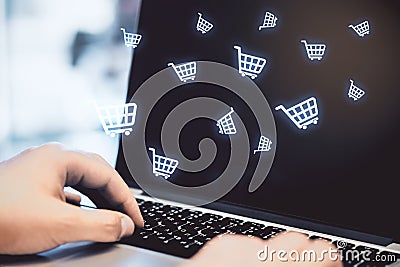 Multiple white shopping carts icons with hands touching the laptop keyboard in the background. Online shopping and purchase Stock Photo