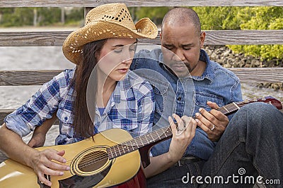 A multiracial couple sits on a deck learning guitar Stock Photo