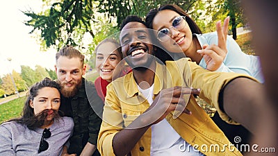 Multiracial group of friends is taking selfie in park sitting on blanket, posing and looking at camera. African American Stock Photo