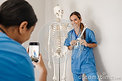 Multiracial women doctors taking photo with skeleton on cellphone Stock Photo