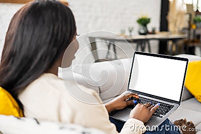 Multiracial young woman spending home leisure with laptop. Calm girl sitting at cozy sofa and looking at the screen in Stock Photo