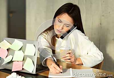 Multitasking at work concept. Woman speaks on phone, writes and drinks coffee Stock Photo