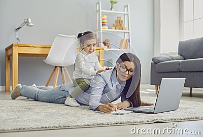 Multitasking for work at home moms. Young woman doing online job on laptop while her daughter sitting on her back Stock Photo