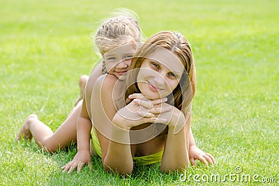 Mum and daughter lie on green lawn in a bikini and look in the frame Stock Photo