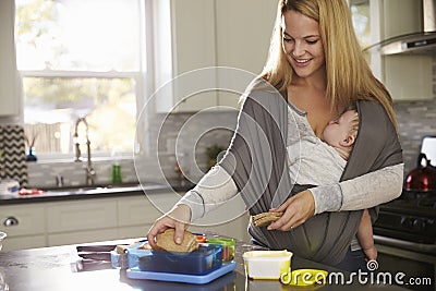 Mum preparing lunchbox while baby sleeps on her in a carrier Stock Photo