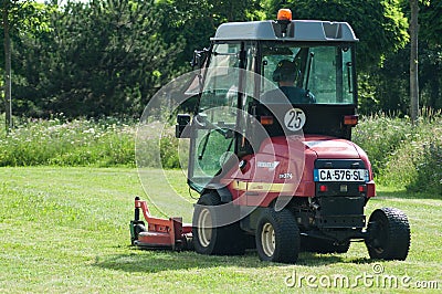 Municipal employee driving Red tractor and lawn mower, shears lawns in urban park Editorial Stock Photo