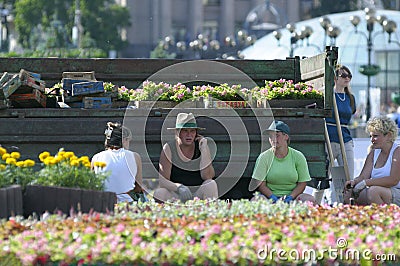 Municipal women workers sitting in the shadow thrown from a truck taking break from caring of a flowerbed Editorial Stock Photo