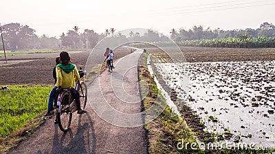 Kids riding a bicycle through a narrow country road passing through green fields Editorial Stock Photo