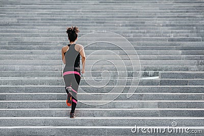 Muscular african american girl in sportswear runs up the stairs in city Stock Photo