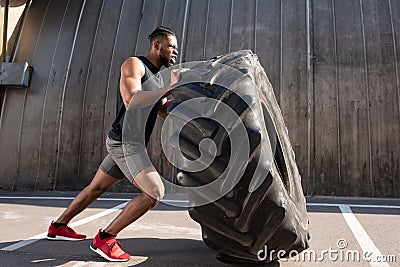 muscular african american sportsman exercising with tire on street Stock Photo