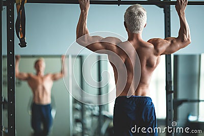 Muscular athlete man making Pull-up in gym. Bodybuilder training in fitness club showing his perfect back and shoulder Stock Photo