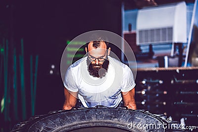 Muscular bearded fitness man moving large tire in the crossfit gym Stock Photo