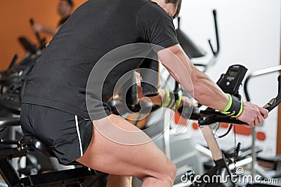 Muscular man biking in the gym, exercising legs doing cardio workout cycling bikes, spinning class. Stock Photo