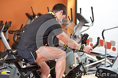 Muscular man biking in the gym, exercising legs doing cardio workout cycling bikes, spinning class. Stock Photo