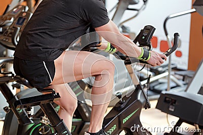Muscular man biking in the gym, exercising legs doing cardio workout cycling bikes, spinning class. Stock Photo