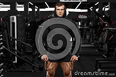 Muscular man with muscle legs in gym. Strong male in black hoodie with big quads Stock Photo