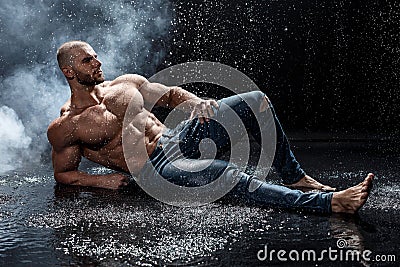 Muscular man under the rain in studio. Sexy male in water drops, abs Stock Photo