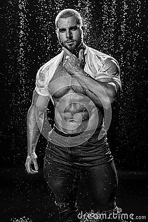 Muscular man under the rain in studio. Sexy male in water drops, abs Stock Photo