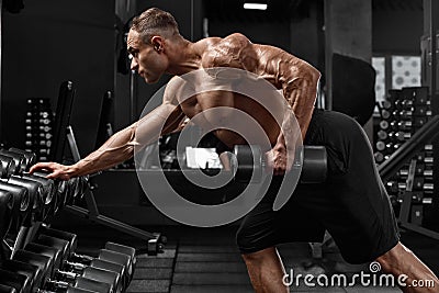 Muscular man working out in gym doing exercise for back. Single arm dumbbell row Stock Photo