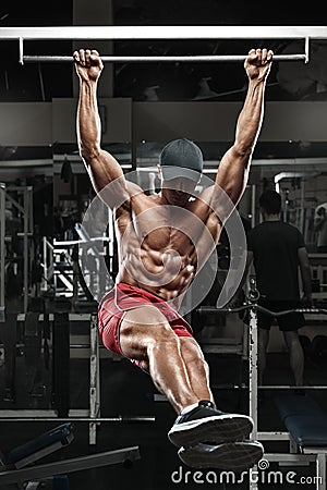 Muscular man working out in gym, doing stomach exercises on a horizontal bar, strong male naked torso abs Stock Photo