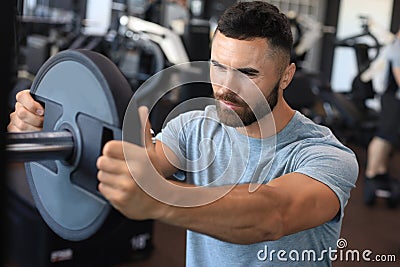 Muscular sporty indian man adding weight on barbell at gym Stock Photo