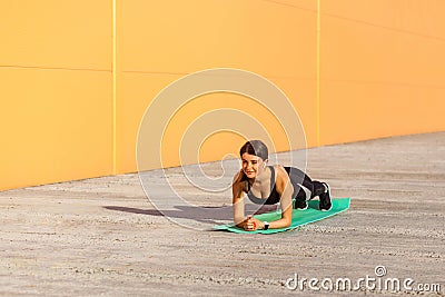 Muscular sporty strong beautiful young athletic woman in black sportwear standing on perfect plank position on elbows on green mat Stock Photo