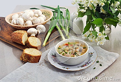 Mushroom soup in a small white bowl. Fresh bread, champignons, green onions on a white table. Stock Photo