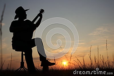 Music concept of black silhouette of man with western hat cowboy and instrument with grass at sunset or sunrise. Musician play Stock Photo