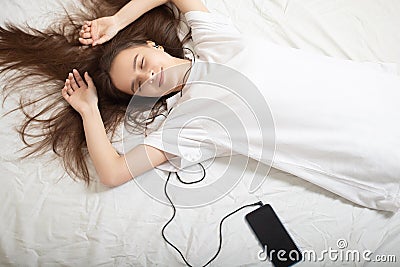 Music Lifestyle. Girl in headphones with a phone with closed eyes lies on the bed Stock Photo