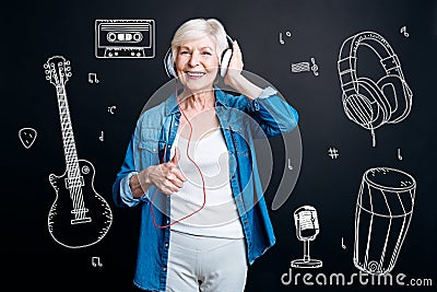 Positive senior woman putting her thumb up while listening to music Stock Photo