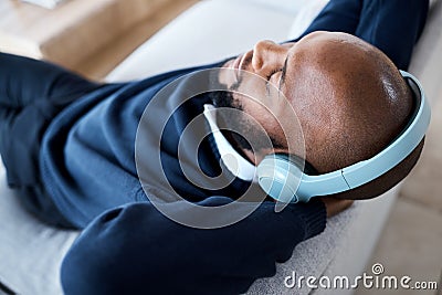 Music top view, headphones and black man on sofa in home living room streaming audio. Meditation, relax technology and Stock Photo