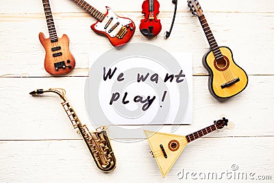 Musical instruments and card with message We want play on wooden background. Stock Photo