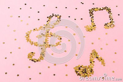 Musical notes of starry golden confetti lying on a pink pastel background. Stock Photo