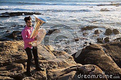 Musician play to musical instrument Tuba on romantic rocky sea shore. Hobby. Stock Photo