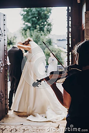 Musician playing on violin while beautiful bride and groom standing in church after wedding matrimony. Elegant string quartet Stock Photo