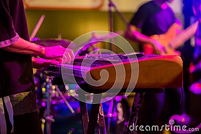 Musician`s hands playing keyboard at a live show on stage with other men playing guitars Stock Photo