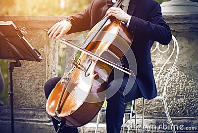 Musician in a suit sitting on a white chair and playing on cello Stock Photo