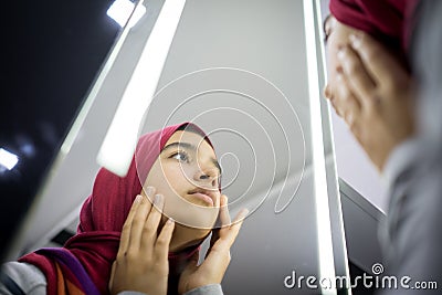 Muslim beautiful girl looking into mirror checking face skin Stock Photo