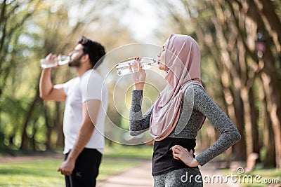 Muslim family in activewear drinking water at park Stock Photo