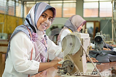 Muslim female employees wearing headscarves smile while working using sewing machines Stock Photo