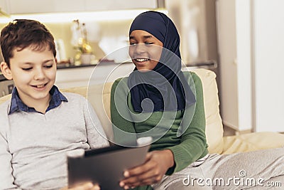 Muslim girl and her caucasina friend sitting at home using digital tablet Stock Photo