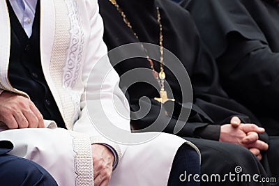 A Muslim mullah in white clothes and a Christian priest in a black cassock are sitting next to each other. The concept of Stock Photo