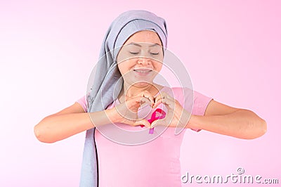 Muslim woman wearing a hijab with a ribbon on her chest shows prevention of breast cancer. On a pink backdrop, breast cancer Stock Photo