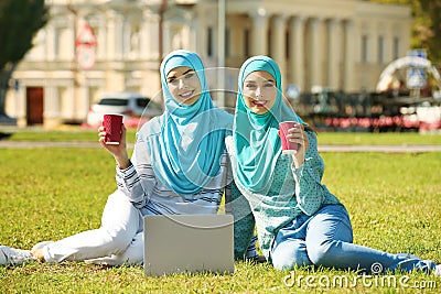 Muslim women in hijabs with laptop sitting on green lawn Stock Photo