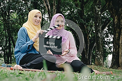 Muslimah holding professional film slate with word ENJOY WEEKEND, movie clapper board at park Stock Photo