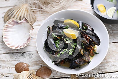 Mussels in wine-butter sauce, sprinkled with parsley, top view. Clams in a bowl, on white wood background. Stock Photo