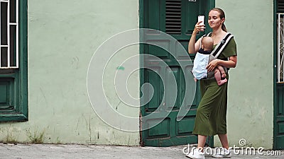 Mutter geht hinunter eine schmale alte Straße mit einem Baby in einem Riemen und schießt ein Video für soziale Netzwerke über ihr stock video Mutter geht hinunter eine schmale alte Straße mit einem Baby in einem Riemen und schießt ein Video für soziale Netzwerke über ihr stock video
