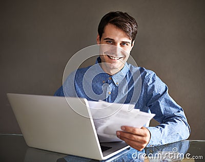 My competitors better watch out. Portrait of a businessman holding paperwork while sitting in front of his laptop. Stock Photo