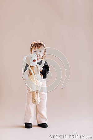 My favorite toy. Cute little 2 years old girl hugging her teddy bear and smiling, decorated beige studio background Stock Photo